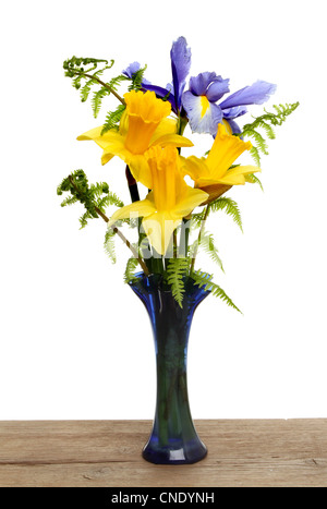 Arrangement of daffodils,fern fronds and a blue iris flower in a vase on a wooden board against a white background Stock Photo