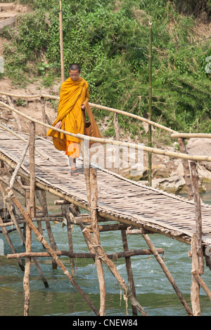 A young Buddhist monk walks across a bamboo bridge in Luang Prabang Laos