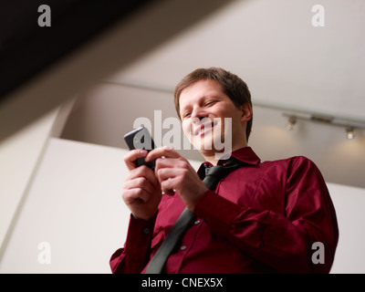 mid adult business man in office, text messaging on mobile phone. Low angle view Stock Photo