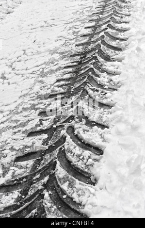 close up of tractor track left behind in snow bound road cleared by snow plough Stock Photo