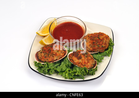 Plate of Cape Cod stuffed clams with breadcrumbs on lettuce with hot sauce and lemons on white background. Stock Photo