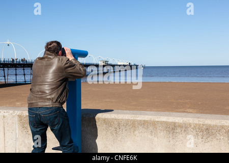 Single caucasian male looking with telescope at sea and pier in Southport England Stock Photo