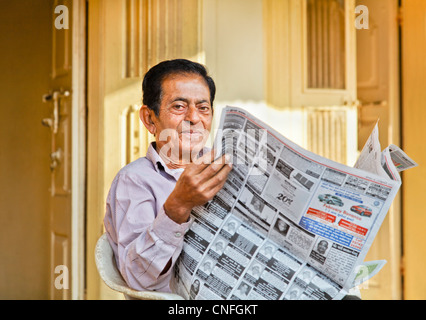 Senior Indian gentleman portrait outside his hinterland village home reading local language morning newspaper on front patio Stock Photo