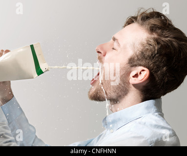 Young man spilling milk from carton, studio shot Stock Photo