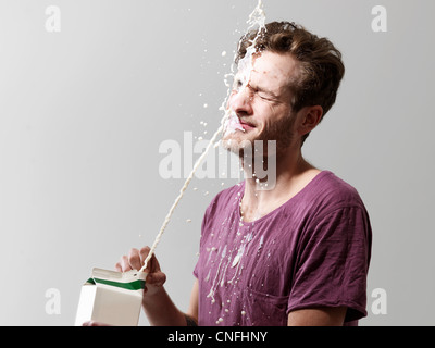 Young man spilling milk from carton, studio shot Stock Photo