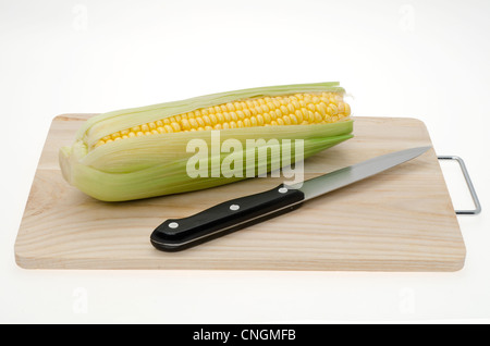 Fresh corn ears or sweetcorn placed on a wooden cutting board - shot in the studio with a white background Stock Photo