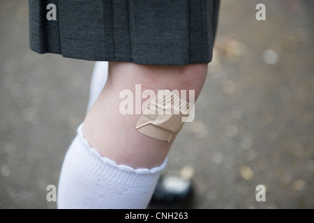 Schoolgirl's knee with a sticking plaster over a cut. Stock Photo