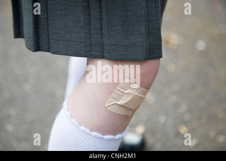 Schoolgirl's knee with a sticking plaster over a cut. Stock Photo