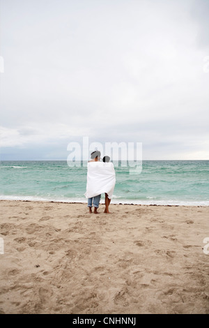 A young couple wrapped in a beach towel standing on the beach Stock Photo