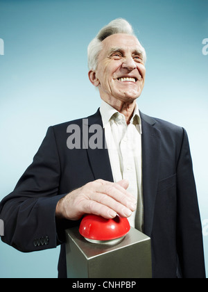 A grinning senior man pushing a red game show buzzer Stock Photo