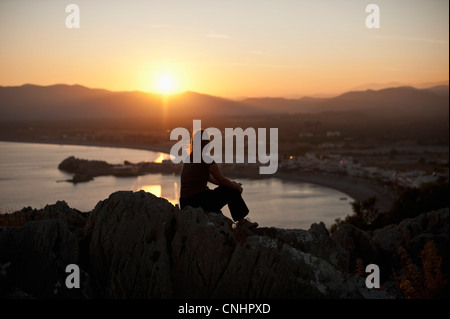 A silhouetted person sitting atop a hill watching the sunset, Rhodes, Greece Stock Photo