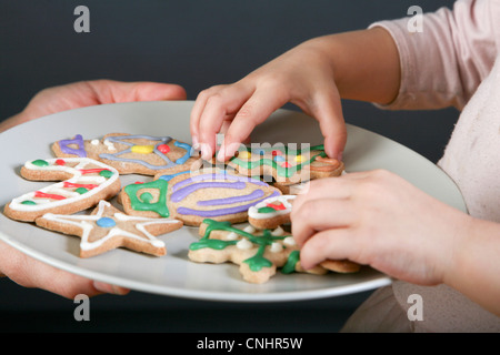 A mother sharing a plate of Christmas cookies with her daughter, focus on hands Stock Photo