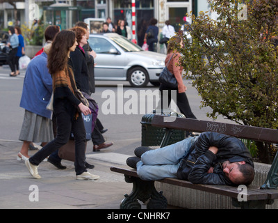 Homeless man sleeping on a bench in the busy streets of Brussels, Belgium Stock Photo