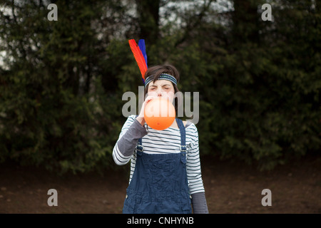 Young woman in headdress, blowing up a balloon Stock Photo