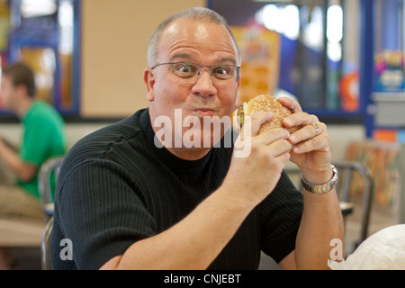 Overweight man eating burger in restaurant Stock Photo