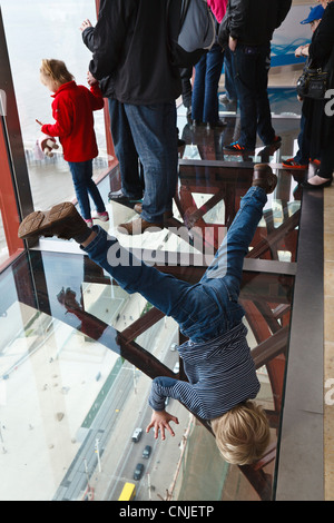 A child finds a way to get a different view from the Blackpool Tower Eye 'Skywalk' by standing on his head. Stock Photo