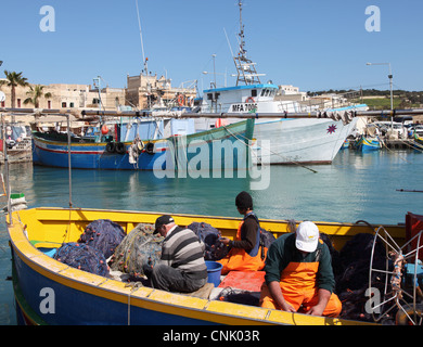 Fishermen mending their nets aboard boat in Marsaxlokk harbour, Malta, Europe Stock Photo