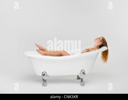Young woman bathing herself in her Victoria + Albert claw foot tub Stock Photo