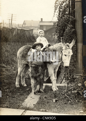 Little Cowboy with Infant Sibling on a Donkey Stock Photo