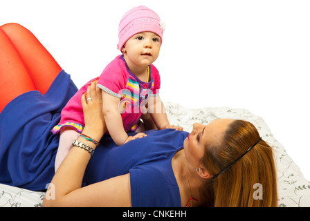 Mother holding happy baby girl on her stomach and lying down on bed against white background Stock Photo