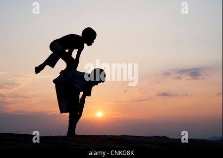 Silhouette of young Indian boys playing leap frog against at sunset. India Stock Photo