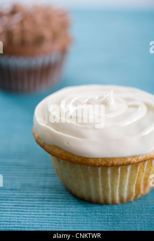 Delicious looking vanilla cupcake with white frosting on teal colored place mat -shallow focus Stock Photo