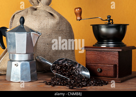 Still life photo of a caffettiera or moka pot with traditional coffee grinder hessian sack and arabica beans in a scoop.