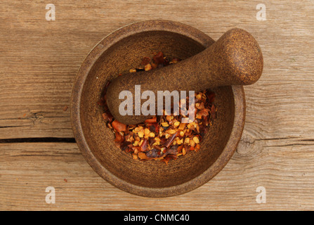 Flaked dried chilli pepper in a pestle and mortar on an old weathered wooden board Stock Photo