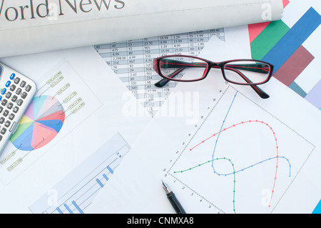 Calculator and pen on top of various business graphs and tables Stock Photo