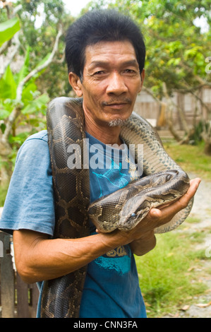 Vertical view of a Vietnamese farmer lovingly holding his pet Boa constrictor snake. Stock Photo