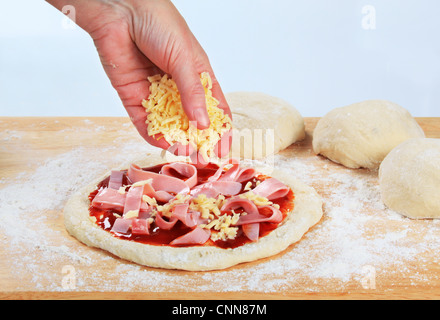 Cook sprinkling shredded cheese over pizza Stock Photo