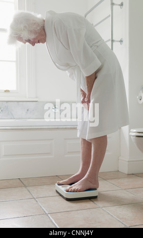 Older woman weighing herself in bathroom Stock Photo