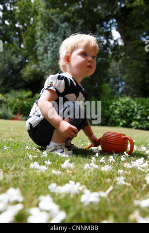 Baby Girl Crouching on Grass in Garden, Farnham, England Stock Photo