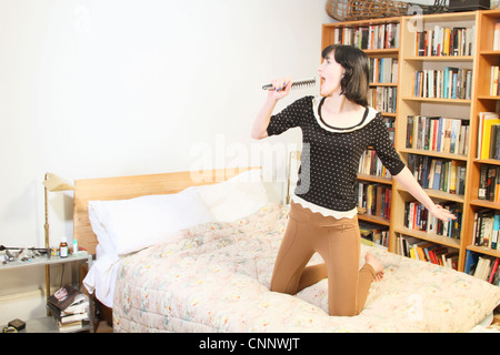 Woman singing into hairbrush on bed Stock Photo