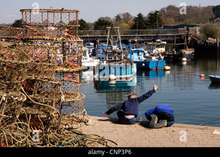 Lymington harbour wall - two small boys fishing for crabs - pulling the line in - leaning over the edge - sunlight and blue sky Stock Photo
