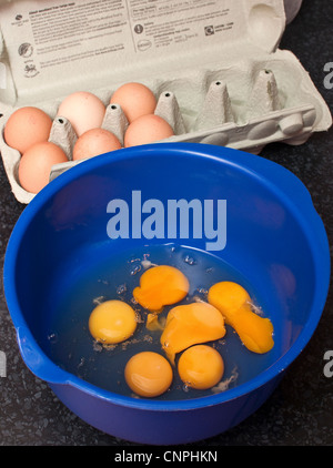 Cracked eggs in a blue bowl ready for whisking six eggs in a box in background Stock Photo