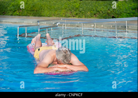 Elderly man floating on air mattress in swimming pool Stock Photo