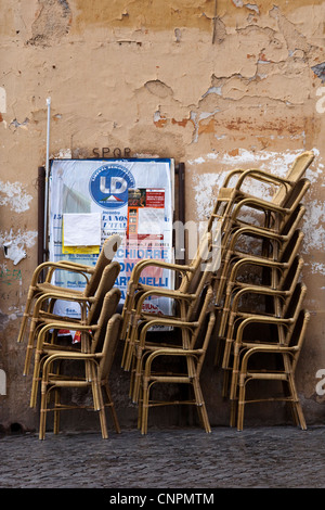 Wicker cafe chairs stacked against a wall with peeling paint and playbill Stock Photo