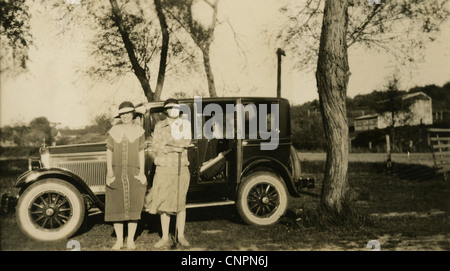 Circa 1920s photograph, two flapper women, one leaning on a golf club, pose by their car. Stock Photo