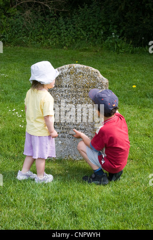 Young boy and girl examining the grave of Hannah Twynnoy in the churchyard of Malmesbury Abbey Stock Photo
