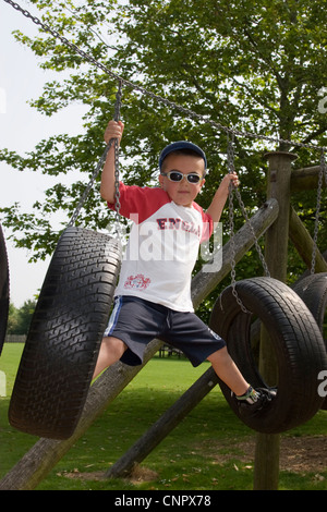 Young boy playing on a swing made from old tyres in an adventure playground Stock Photo