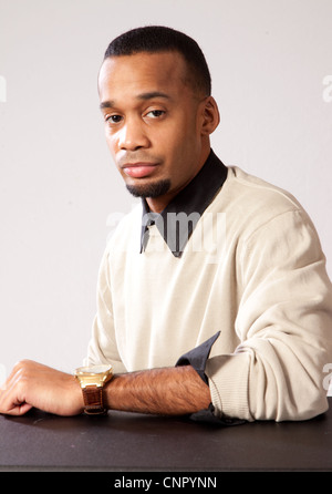 Handsome young black man with pensive expression looking at the camera and sitting with his forearm on a table Stock Photo