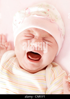 Closeup portrait of cute little baby girl crying in pink pajama & hat Stock Photo