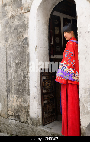 Profile of a new bride wearing her red wedding dress in the doorway of an ancient Hongcun village building Anhui Province China Stock Photo