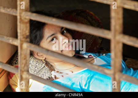 Rural scene in Gujarat India of young lady with pretty eyes catching sunrays through a grilled window opening Stock Photo