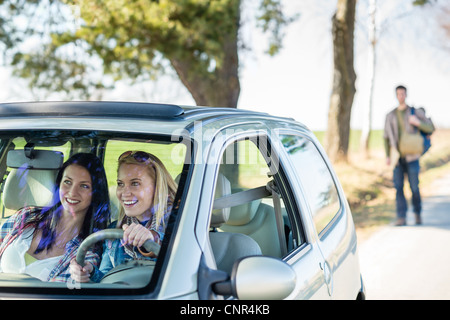 Two women happy in car taking handsome hitch-hiker road trip Stock Photo