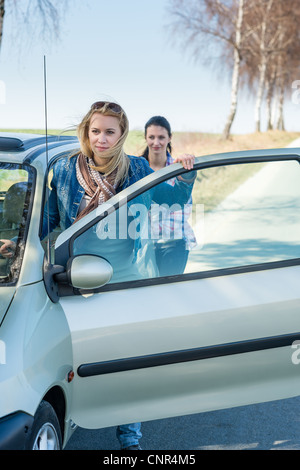 Vehicle breakdown two young women pushing car down the road Stock Photo