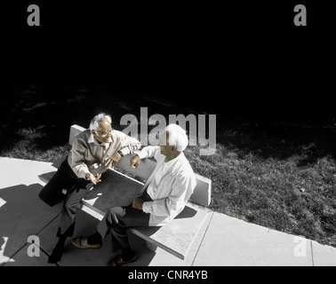 two elderly ethnic men sitting on a bench talking Stock Photo