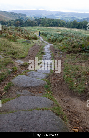 Tiny Figure Walking on Granite Stone Pathway Coming Down from Stanage Edge, Derbyshire, Dark Peak, Peak District, UK Stock Photo