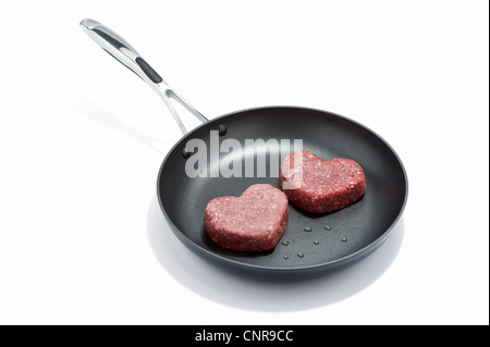 Two heart shaped beef burgers in a frying pan Stock Photo